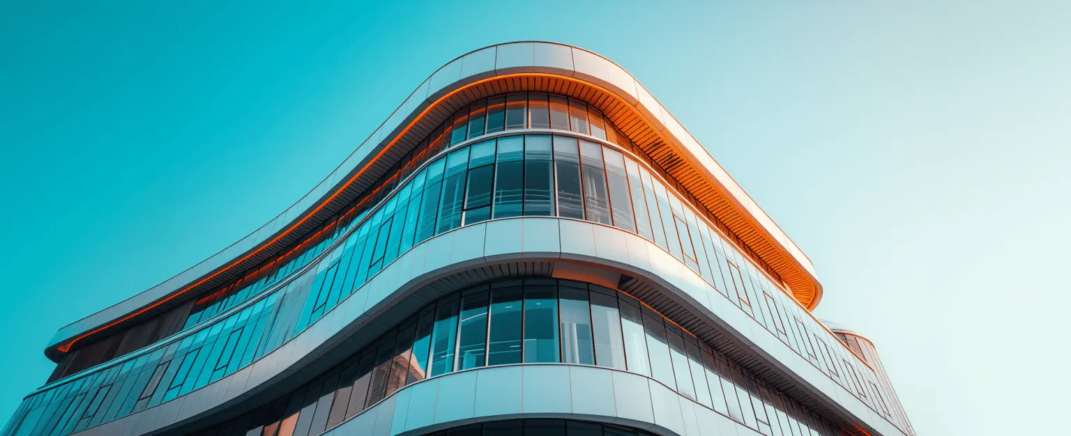 Das Bild zeigt ein modernes, mehrstöckiges Gebäude mit einer charakteristischen, geschwungenen Form. Das Gebäude hat große, gläserne Fenster und sanfte, fließende Linien, die ihm ein elegantes und zeitgemäßes Aussehen verleihen. Die Struktur des Gebäudes hebt sich vor dem klaren, blauen Himmel ab, was seine visuelle Attraktivität unterstreicht.
